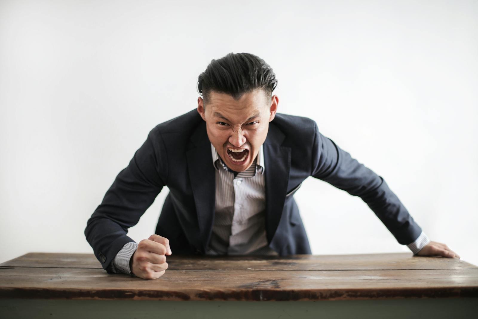 Businessman expressing intense anger at a table, showcasing emotional tension and frustration.