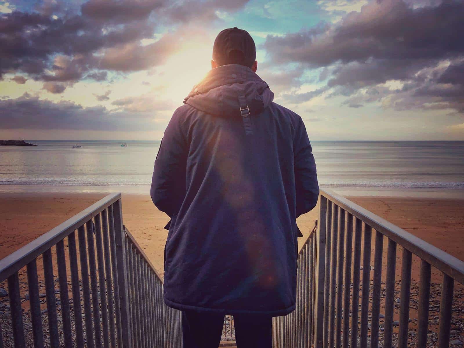 Solitary figure on a beach at sunset, contemplating the horizon in peaceful solitude.