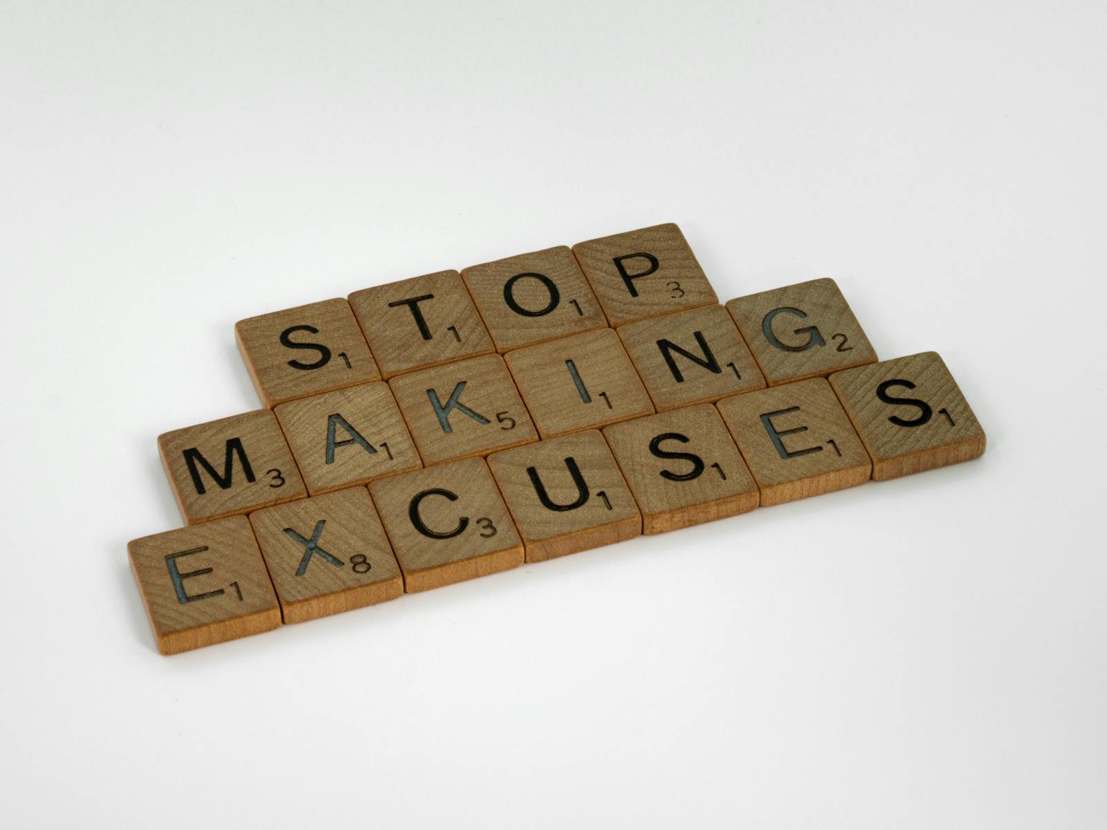 Motivational wooden tiles spelling stop making excuses against a clean white background.