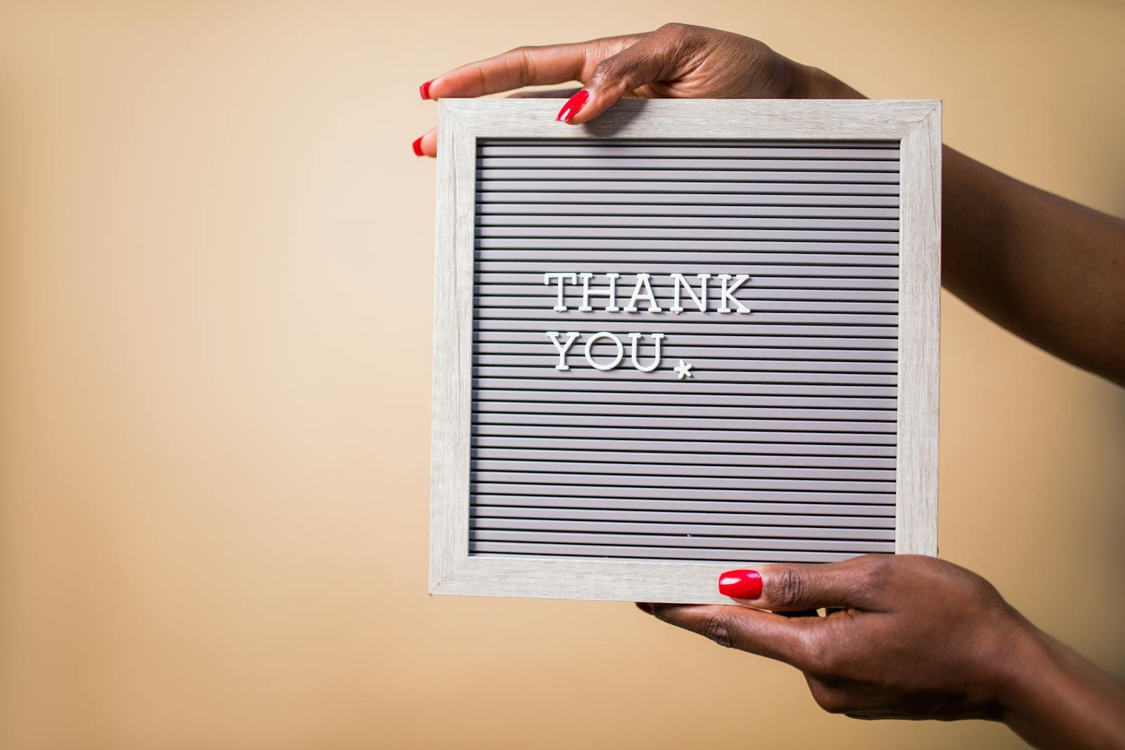 Elegant letter board displaying thank you held by a person with vibrant red nails.