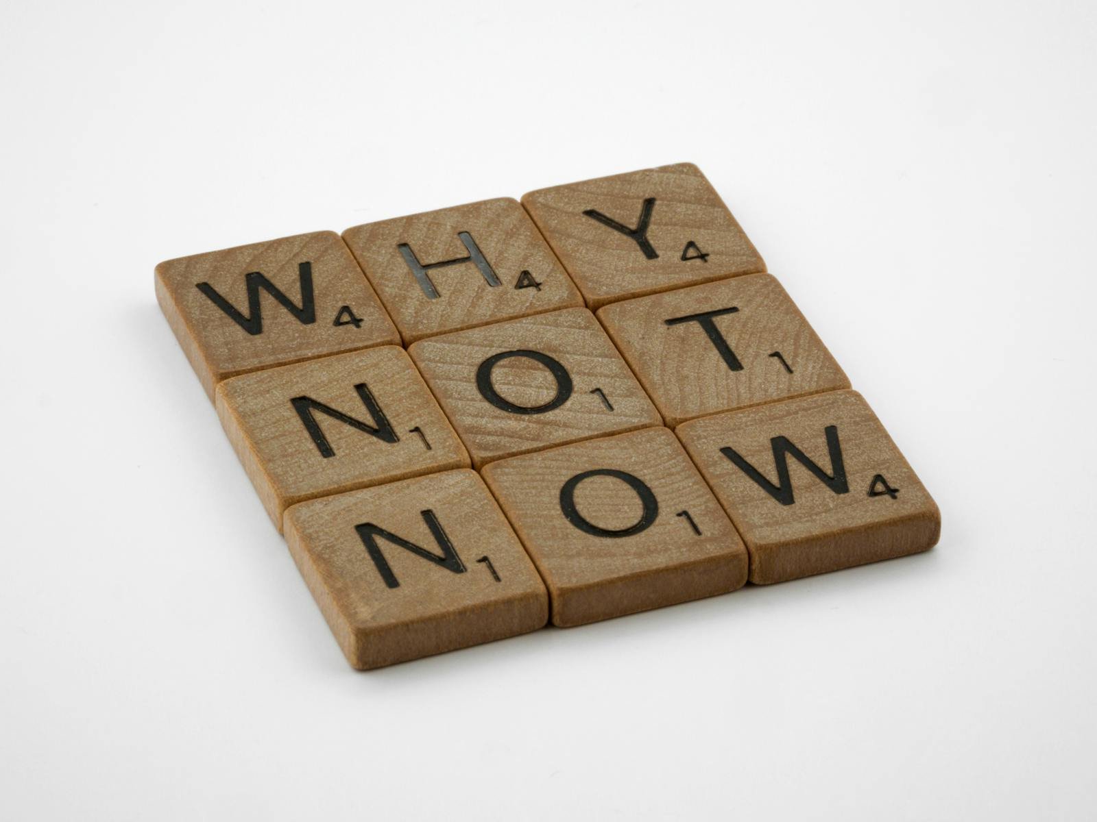 Wooden letter tiles spell why not now, inspiring immediate action and motivation.