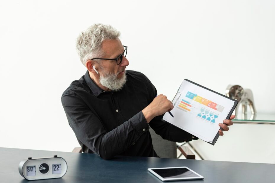 Older man home showing graph notepad with tablet desk