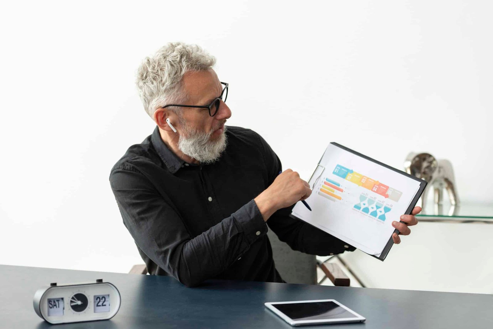 Older man home showing graph notepad with tablet desk