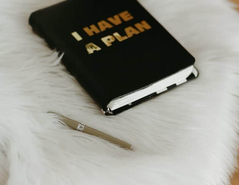 Stylish home office setup featuring a notebook with 'i have a plan' text and a pen on a fluffy white chair.