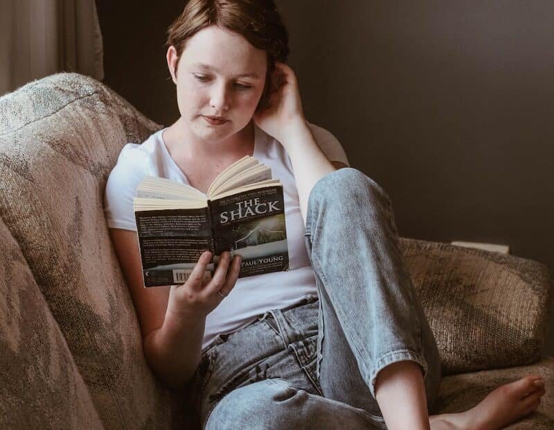 Woman sitting on sofa while reading book inside room, 3 self help books