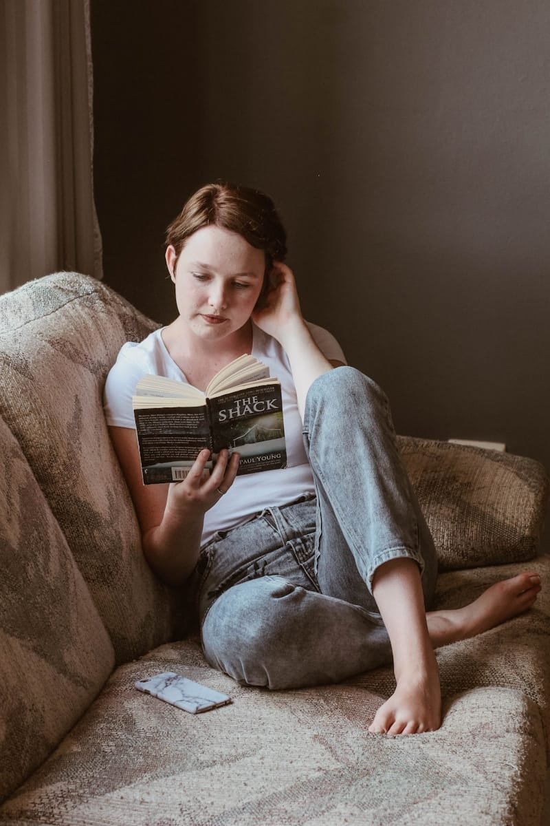 Woman sitting on sofa while reading book inside room, 3 self help books