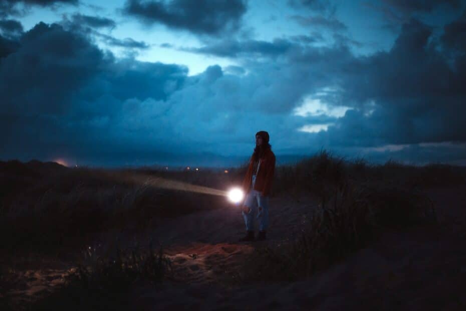 A person standing on a dirt path with the sun shining through clouds