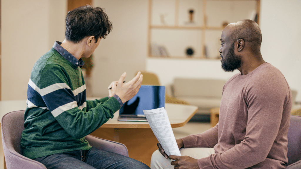 A man holding a piece of paper and talking to another man