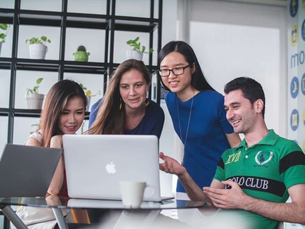 Four people watching on white macbook on top of glass-top table